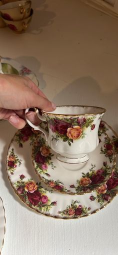 a person is holding onto a teacup and saucer on a table with other dishes