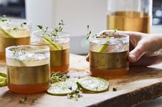 three glasses filled with different kinds of drinks on top of a wooden cutting board next to sliced limes