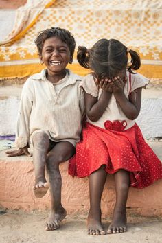 two young children sitting on a ledge with their hands covering their faces and smiling at the camera