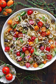 a white bowl filled with pasta and vegetables on top of a wooden table next to tomatoes