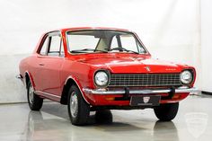 an old red car is parked in a room with a white wall and logo on it