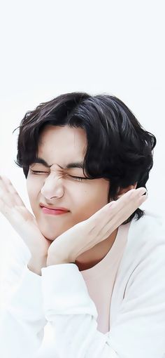 a woman with black hair and white shirt holding her hand up to her face while looking at the camera