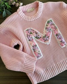 a pink sweater with a bow on the front and floral appliques on the back