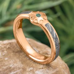 a close up of a gold ring on top of a rock with green leaves in the background