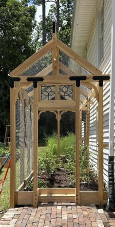 a small wooden house with a chicken cage on the front porch and garden in the back