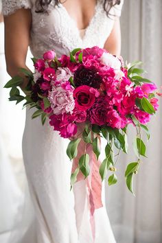 a bride holding a bouquet of pink and purple flowers with greenery in her hand