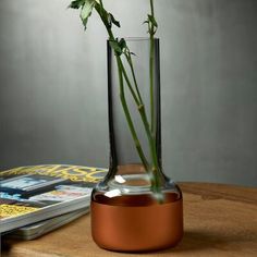 a single rose in a glass vase on a table next to a magazine and magazines