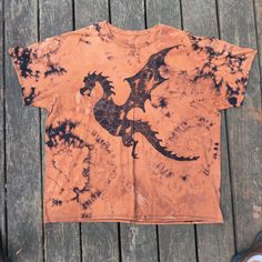 an orange shirt with a black dragon on it sitting on a wooden floor next to shoes