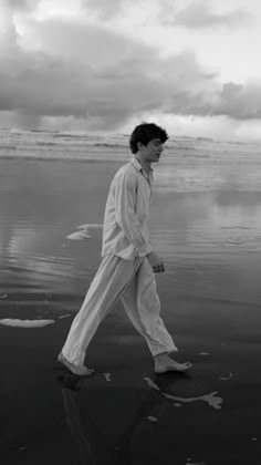 black and white photograph of man walking on beach with ocean in the backgroud