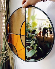 a hand holding a circular stained glass mirror in front of a houseplant and potted plant