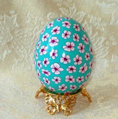 an egg with flowers painted on it is sitting on a gold plated stand against a white background