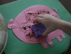 a child's hand holding a sponge on top of a pink paper plate with an elephant design