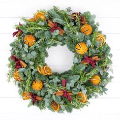 a wreath with oranges and greenery hanging on a white wooden wall behind it