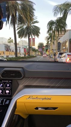 the dashboard of a car with palm trees in the back ground and buildings on either side