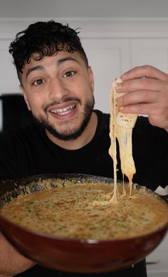 a man is holding a bowl of soup with cheese being drizzled over it