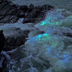 the waves are crashing against the rocks on the beach at night, with green light coming from them