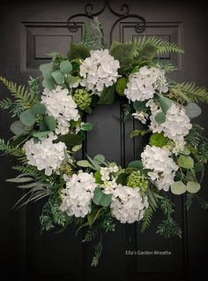 a wreath with white flowers and greenery is hanging on the front door's black door