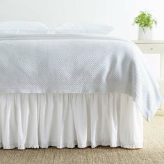 the bed is made with white sheets and ruffled bedskirt, along with a potted plant