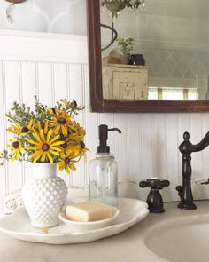 a bathroom sink with soap, soap dish and flowers in the vase next to it