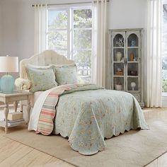 a bed in a bedroom with a white headboard and window behind it, next to a bookcase