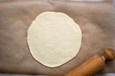 an uncooked pizza dough sitting on top of a piece of parchment paper next to a rolling pin