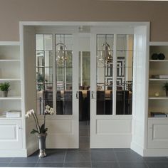 an empty room with two glass doors and shelves on either side of the door is a vase with flowers in it