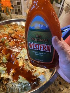 a person holding a bottle of ketchup in front of a plate of food