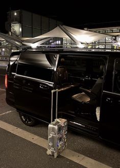 a black van with its door open and luggage on the ground in front of it