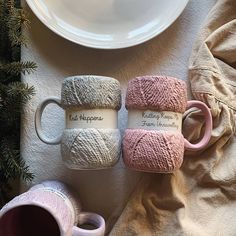 three knitted mugs sitting on top of a table next to a white plate