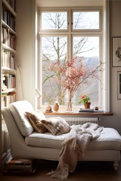 a white couch sitting in front of a window next to a book shelf filled with books