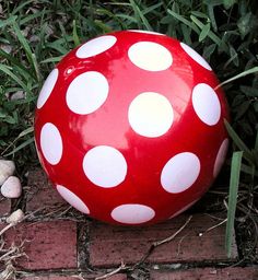 a red and white polka dot ball sitting on the ground next to some green grass