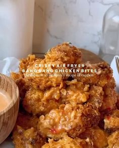 a plate full of fried food next to a wooden bowl with dipping sauce on it