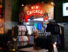 a man standing in front of a clothing store at night with neon signs above it