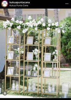 an outdoor wedding ceremony with white flowers and framed pictures on the side of a gold shelving