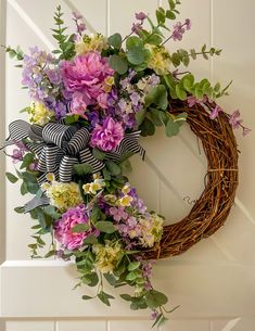 a wreath with purple and white flowers hanging on a door