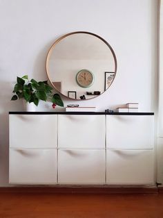 a white dresser topped with a mirror and a plant next to it on top of a hard wood floor