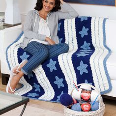 a woman sitting on top of a couch next to a blue and white blanket