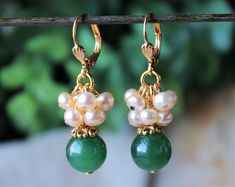 "This lovely pair of earrings features a beautiful emerald green jade gemstone, which are accented with an ornate pewter bead cap, plated in 24 karat gold. This striking color combination is offset with small clusters of champagne freshwater pearls. Hanging from a surgical steel lever-back, it measures 1 ¼\" in length. Earrings are light weight and sway gracefully as you move about your day. Also available in sterling silver plate. Available with sculpted clip-on earrings top, please see last ph Green Jade Earrings For Wedding, Wedding Jewelry With Natural Jade Stones, Green Emerald Earrings With Pearl Drop, Green Jade Earrings For Anniversary, Green Natural Stone Earrings For Wedding, Green Natural Stones Earrings For Wedding, Verde Jade, Verde Smeraldo, Jewelry Design Inspiration