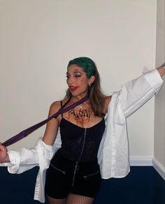 a woman with green hair and makeup is holding two ties in her hands while standing next to a wall