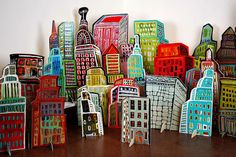 a group of colorful paper cut buildings on a wooden table next to a white wall