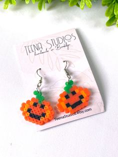 a pair of orange and black beaded pumpkin earrings sitting on top of a card