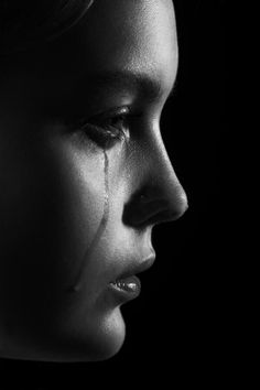 black and white photograph of a woman with tears on her face in the dark