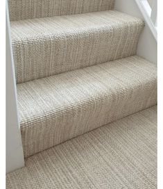 a carpeted staircase with white handrails and beige carpet on the bottom step