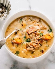 a white bowl filled with soup next to a spoon on top of a marble counter