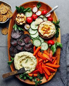 a platter with carrots, radishes, hummus and crackers