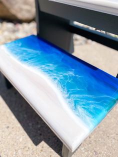 a bench sitting on top of a beach covered in blue and white paint next to the ocean