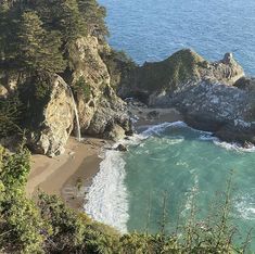 the beach is surrounded by large rocks and trees near the water's edge with waves crashing on it