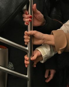 two hands holding onto the bars of a metal railing on a subway train or bus