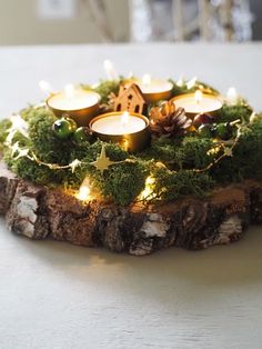 a candle holder made out of wood with moss and lit candles in it on a table