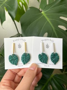 two green leaf shaped earrings are shown in front of a card with the words poppy hill on it